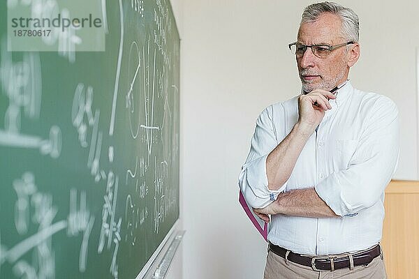 Älterer Mathelehrer  der an die Tafel denkt