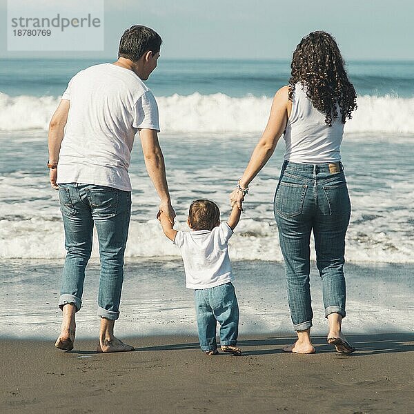Glückliche Familie mit Baby beim Strandspaziergang mit Blick aufs Meer