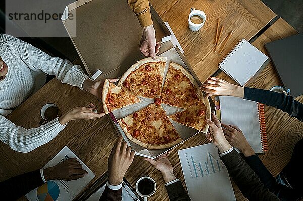 Draufsicht auf Kollegen beim Pizzaessen in der Pause einer Bürobesprechung