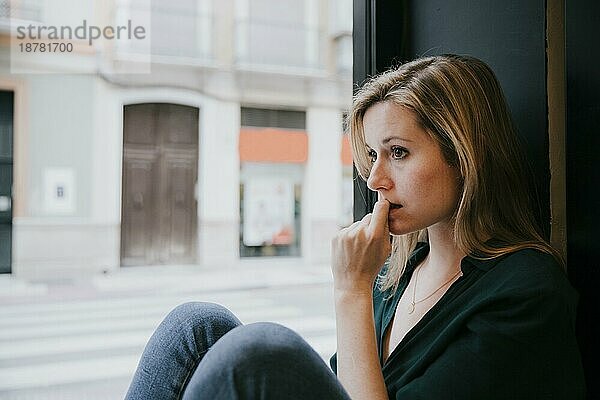Frau denkt in der Nähe des Fensters eines Cafés