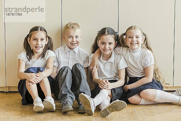 Fröhliche Kinder sitzen auf dem Boden Schule
