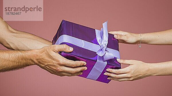 Close up Paar hält eingewickelt lila Geschenk-Box gegen farbigen Hintergrund