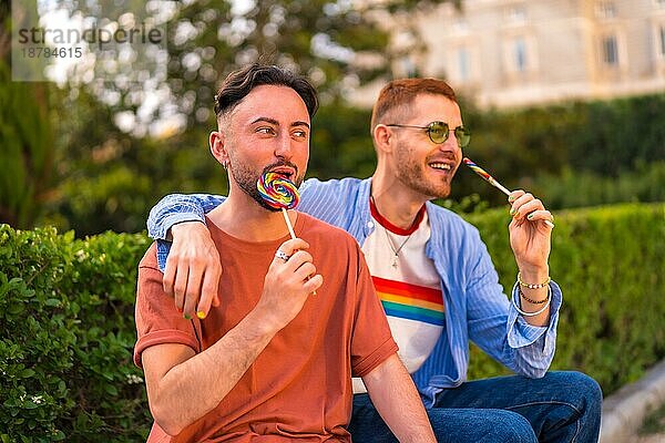 Porträt eines lächelnden Hochzeitspaares  das einen Lutscher im Park bei Sonnenuntergang in der Stadt isst. Vielfalt und lgbt Lebensstil Konzept