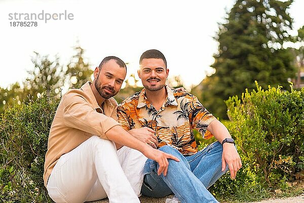 Romantisches Porträt von Homosexuell Jungvermählten sitzen und Spaß bei Sonnenuntergang in einem Park in der Stadt. Vielfalt und lgbt Konzept