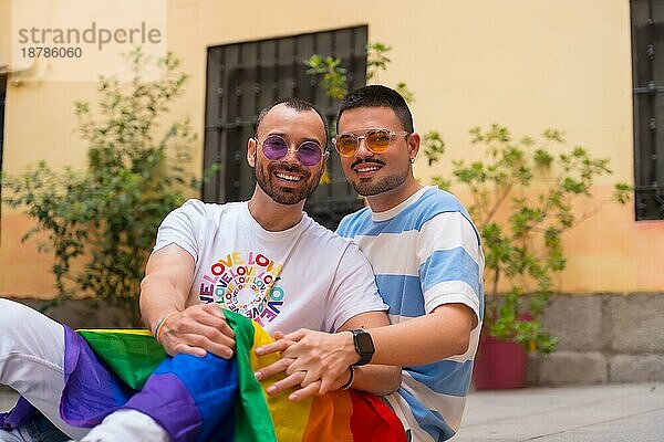 Porträt von Homosexuell männliches Paar sitzt auf dem Boden lächelnd auf Stolz Partei mit Regenbogenflagge  lgbt Konzept