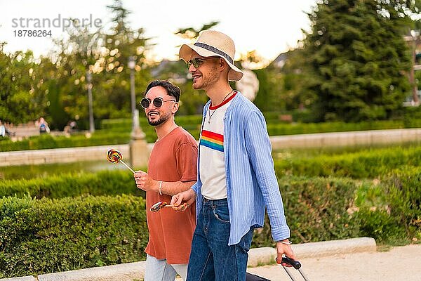 Männliche Touristen Homosexuell Freunde mit einem Koffer in den Park bei Sonnenuntergang in der Stadt den Besuch der Stadt für den Stolz Festival. lgbt Konzept