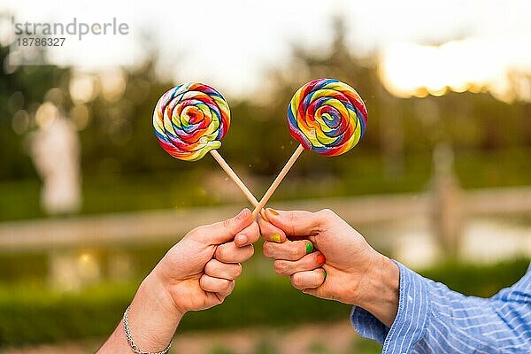 Hand von Homosexuell Freund Männer essen einen Lutscher im Park auf Sonnenuntergang in der Stadt. lgbt Konzept