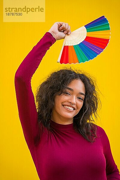 Porträt einer lateinischen Frau mit einem Regenbogen lgbt Fan auf einem gelben Hintergrund