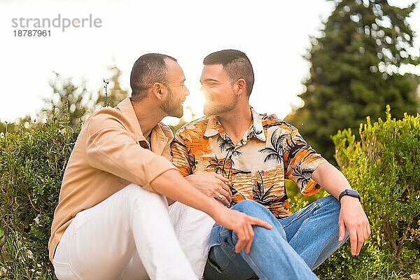 Romantisches Porträt von Homosexuell Jungvermählten sitzen küssen bei Sonnenuntergang in einem Park in der Stadt. Vielfalt und lgbt Konzept