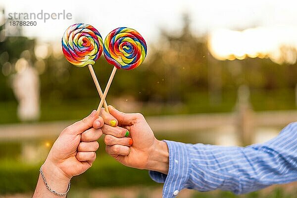 Hand von Homosexuell Freund Männer essen einen Lutscher im Park auf Sonnenuntergang in der Stadt. lgbt Konzept