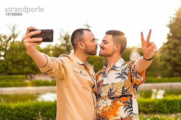 Homosexuelles Paar macht ein Selfie und küsst sich bei Sonnenuntergang in einem Park in der Stadt. Vielfalt und lgbt Konzept