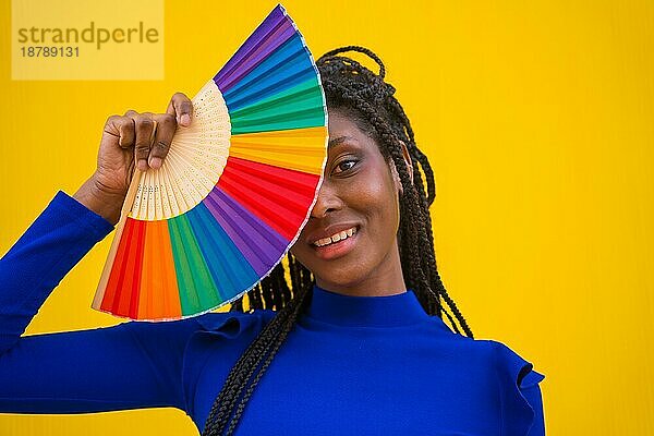 Eine schwarze ethnische Frau mit einem Regenbogen lgbt Fan auf einem gelben Hintergrund
