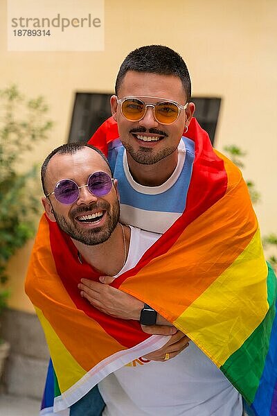 Porträt von Homosexuell männliches Paar Reiten auf dem Rücken lächelnd bei Pride Party mit Regenbogenflagge  lgbt Konzept