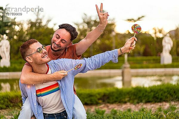 Homosexuell Freunde spielen und ein kletterte auf dem Rücken läuft essen einen Lutscher im Park auf Sonnenuntergang in der Stadt. lgbt Konzept