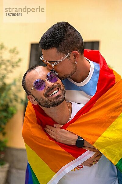 Porträt eines Paares homosexueller Männer  die auf dem Dach reiten und sich bei einer Pride Party mit Regenbogenfahne einen kleinen Kuss geben  lgbt Konzept