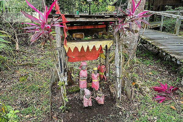 Familie mit Ahnenfigur in einem Garten des Sarawak Cultural Village. Hier werden die verschiedenen ethnischen Gruppen und die lokale Kultur der Stämme von Sarawak vorgestellt