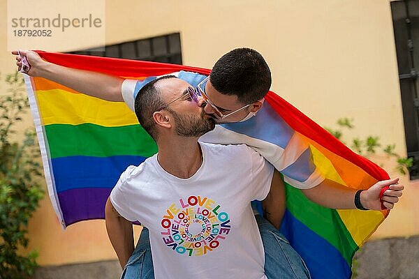 Homosexuelles männliches Paar reitet auf dem Rücken und küsst sich bei einer Pride Party mit Regenbogenfahne  lgbt Konzept