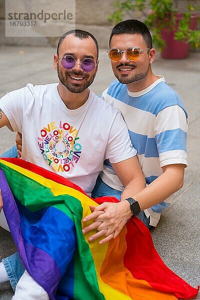 Porträt von Homosexuell männliches Paar sitzt auf dem Boden lächelnd auf Stolz Partei mit Regenbogenflagge  lgbt Konzept