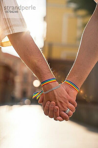 Detail der haltenden Hände eines Paares von homosexuellen Männern mit der Regenbogenflagge auf der Pride Party in der Stadt  lgbt Konzept