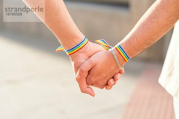 Detail der haltenden Hände eines Paares von homosexuellen Männern mit der Regenbogenflagge auf der Pride Party in der Stadt  lgbt Konzept