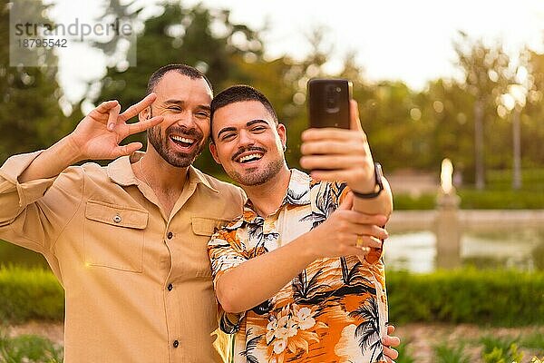 Homosexuelle Freunde machen einen Videoanruf lachend bei Sonnenuntergang in einem Park in der Stadt. Vielfalt und lgbt Konzept