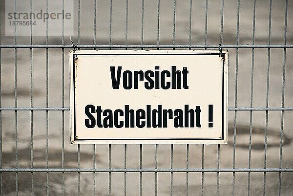 Beschriftung an einem Zaun  der vor Stacheldraht warnt  im Hamburger Hafen. Einige Firmen schützen ihr eigenes Grundstück mit Stacheldraht. Am Zaun befindet sich eine Warnung