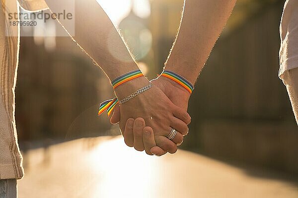 Detail der haltenden Hände eines Paares von homosexuellen Männern mit der Regenbogenflagge bei der Pride Party in der Stadt bei Sonnenuntergang  lgbt Konzept