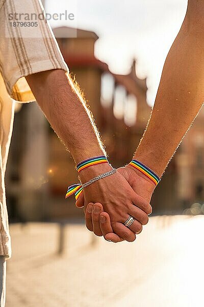 Detail der haltenden Hände eines Paares von homosexuellen Männern mit der Regenbogenflagge bei der Pride Party in der Stadt bei Sonnenuntergang  lgbt Konzept