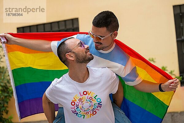 Homosexuelles männliches Paar reitet auf dem Rücken und küsst sich bei einer Pride Party mit Regenbogenfahne  lgbt Konzept