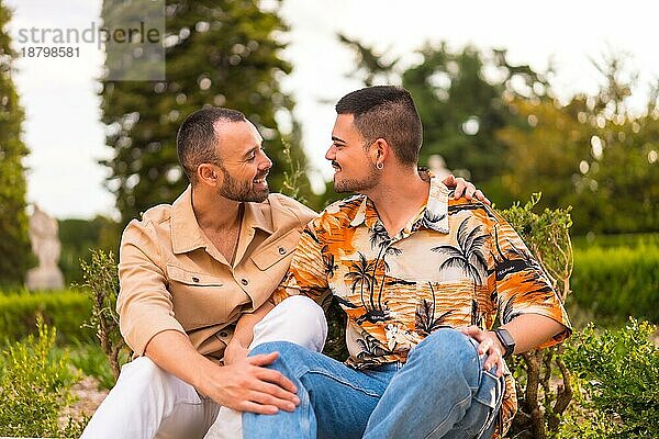Romantisches Porträt von Homosexuell Jungvermählten sitzen küssen bei Sonnenuntergang in einem Park in der Stadt. Vielfalt und lgbt Konzept