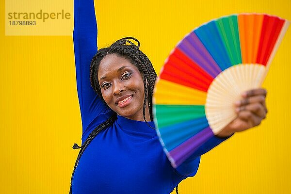 Porträt einer attraktiven schwarzen ethnischen Frau mit einem Regenbogen lgbt Fan auf einem gelben Hintergrund