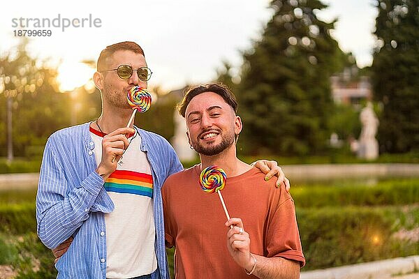 Porträt des lachenden Hochzeitspaares beim Essen eines Lutschers im Park bei Sonnenuntergang in der Stadt. Vielfalt und lgbt Konzept