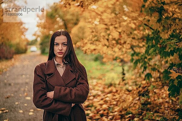 Junge schöne Frau in braunem Mantel im Park im Herbst