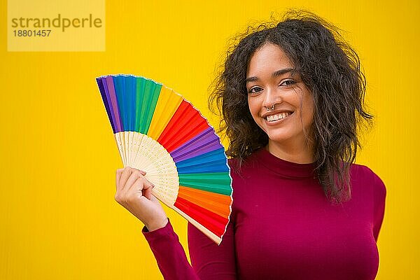 Porträt einer lateinischen Frau mit einem Regenbogen lgbt Fan auf einem gelben Hintergrund