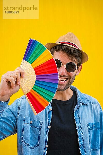 Porträt eines kaukasischen Mannes mit einem Regenbogen lgbt Fan auf einem gelben Hintergrund