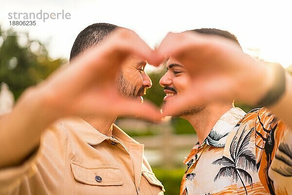Porträt von Homosexuell Freund und Freundin machen Herz oder Liebe Geste bei Sonnenuntergang in einem Park in der Stadt. Vielfalt und lgbt Konzept