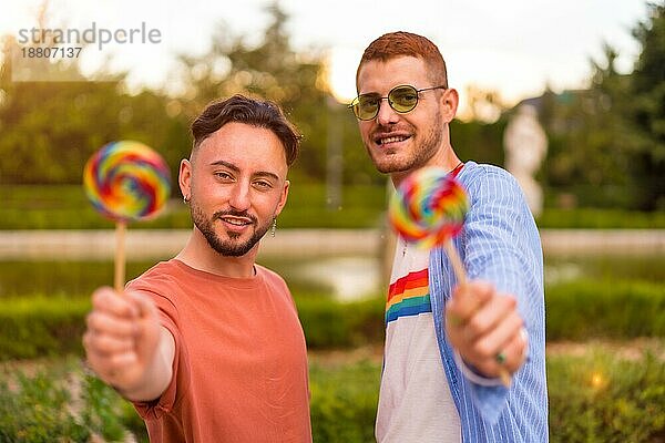 Porträt eines schwulen Hochzeitspaares  das einen Lutscher im Park bei Sonnenuntergang in der Stadt isst