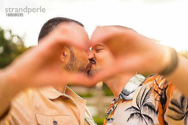 Porträt von Homosexuell Freund und Freundin machen das Herz oder Liebe Geste küssen bei Sonnenuntergang in einem Park in der Stadt. Vielfalt und lgbt Konzept