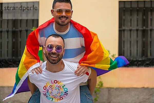 Homosexuelles männliches Paar reitet auf Rücken an Rücken bei Pride Party mit Regenbogenflagge  lgbt Konzept