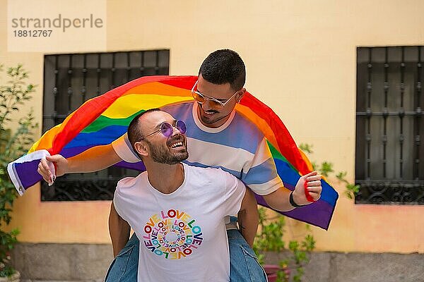 Homosexuelles männliches Paar reitet auf Rücken an Rücken bei Pride Party mit Regenbogenflagge  lgbt Konzept