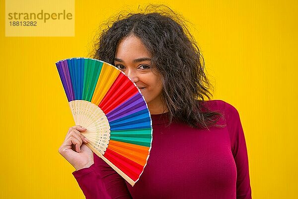 Porträt einer lateinischen Frau lächelnd mit einem Regenbogen lgbt Fan auf einem gelben Hintergrund