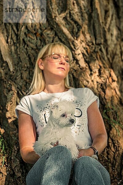 Frau mit kleinem Hund entspannt sich unter einem Baum