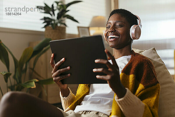 Cheerful young woman wearing wireless headphones watching movie on tablet PC at home