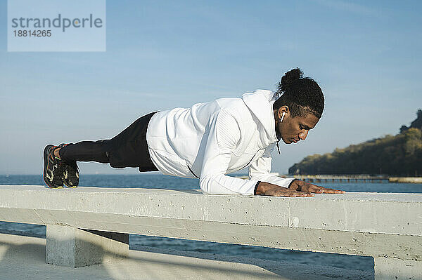Sportler übt an einem sonnigen Tag die Plankenposition auf dem Geländer