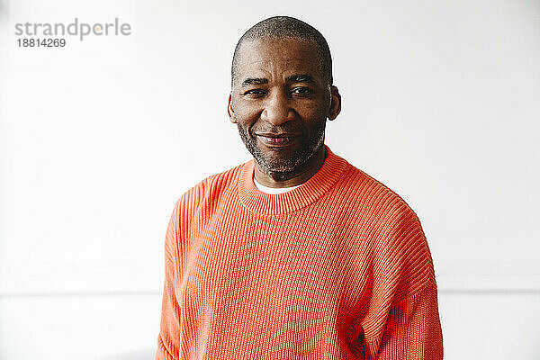 Mature man wearing orange sweater in front of white wall