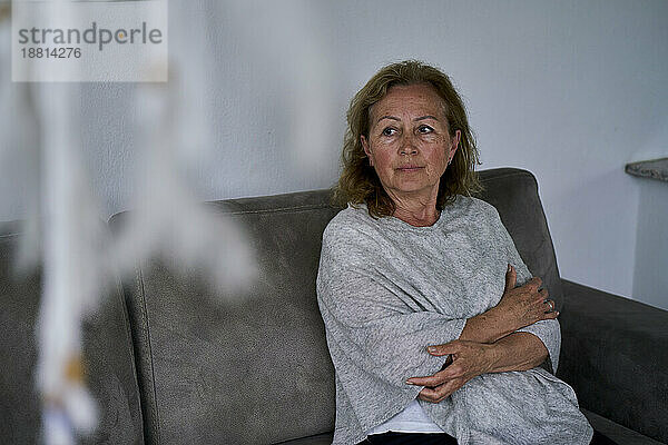 Thoughtful senior woman sitting with arms crossed at home