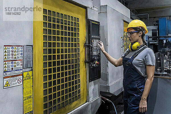 Ingenieur mit Schutzhelm bedient CNC-Maschine in moderner Fabrik