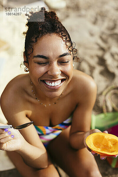 Glückliche Frau mit geschlossenen Augen hält Mango am Strand