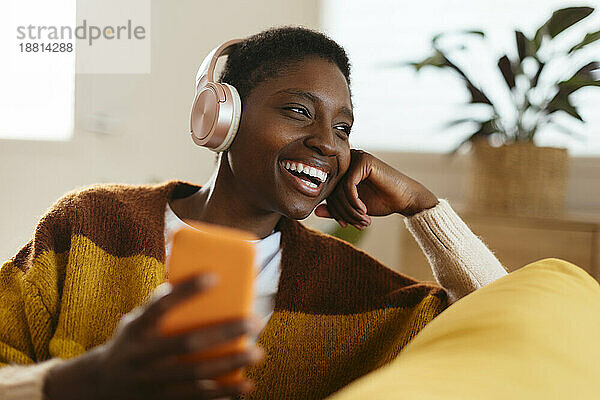 Glückliche junge Frau mit kabellosen Kopfhörern sitzt zu Hause
