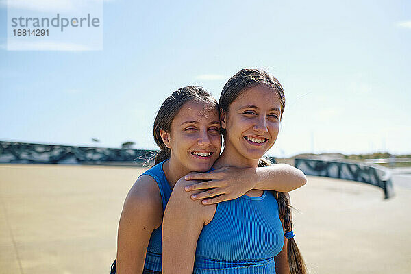 Glückliche Schwestern stehen an einem sonnigen Tag im Skateboardpark